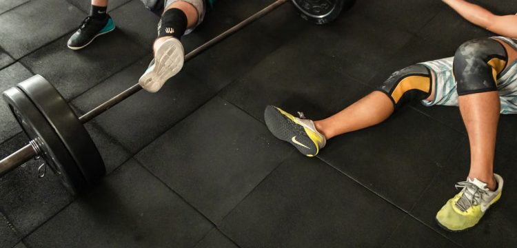 Athletes resting on a gym floor beside heavy barbells after an intense weightlifting session.
