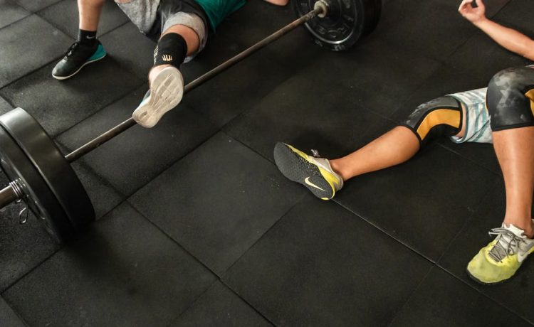 Athletes resting on a gym floor beside heavy barbells after an intense weightlifting session.